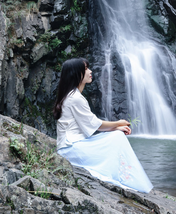 Woman sitting on the rockside of a river with a waterfall