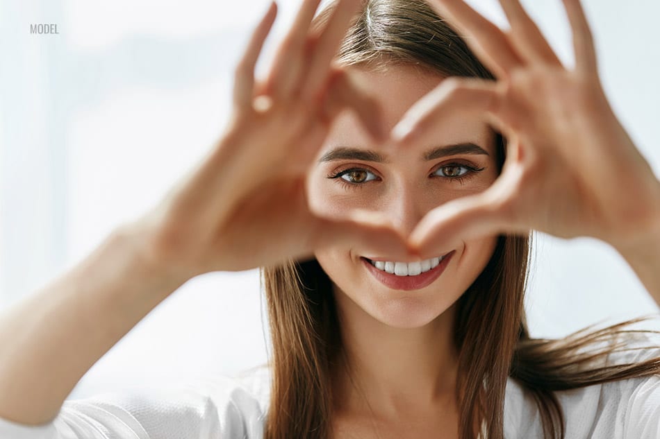 Portrait of a young woman smiling and looking through her hands in the shape of heart